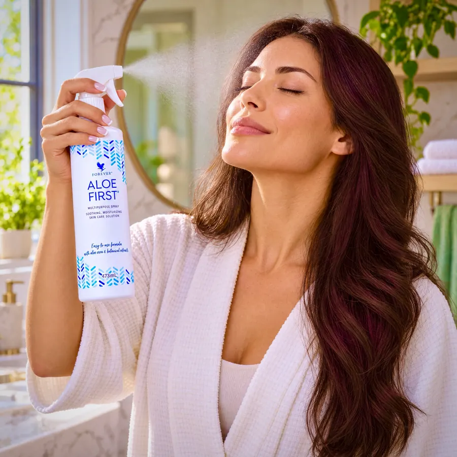 Femeie tânără pulverizând Aloe First pe față dimineața, în fața oglinzii din baie